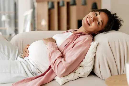 Schwangere Frau, die sich zu Hause auf dem Sofa entspannt und den Bauch berührt